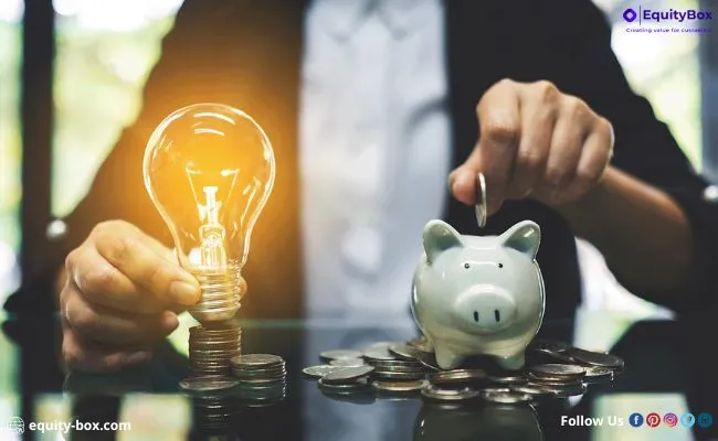 A person holding a glowing lightbulb and dropping a coin into a piggy bank